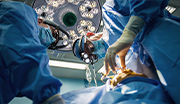 Low-angle view of Navy surgeons in blue scrubs and masks performing surgery under bright overhead lights; surgical instruments visible.