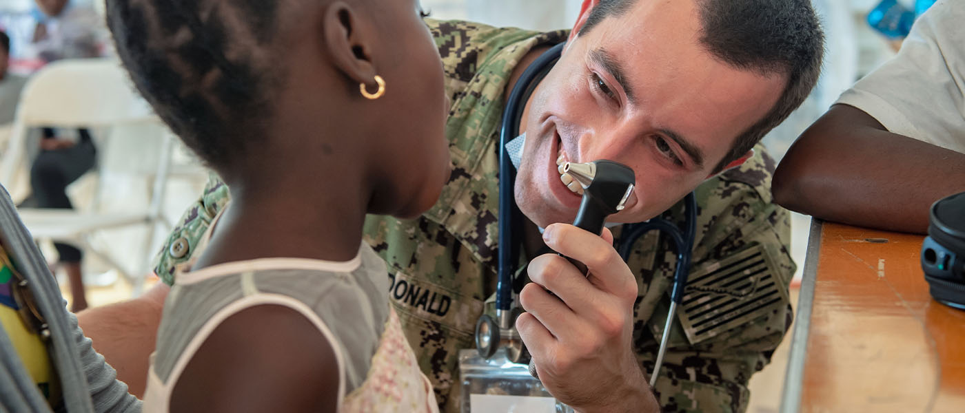 Navy physician smiling while examining a young girl's ear with an otoscope during a humanitarian mission in Haiti.