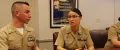 Navy Legalmen in khaki uniforms discuss legal matters at a table with an open book, a 'National Moot Court Competition' poster behind them